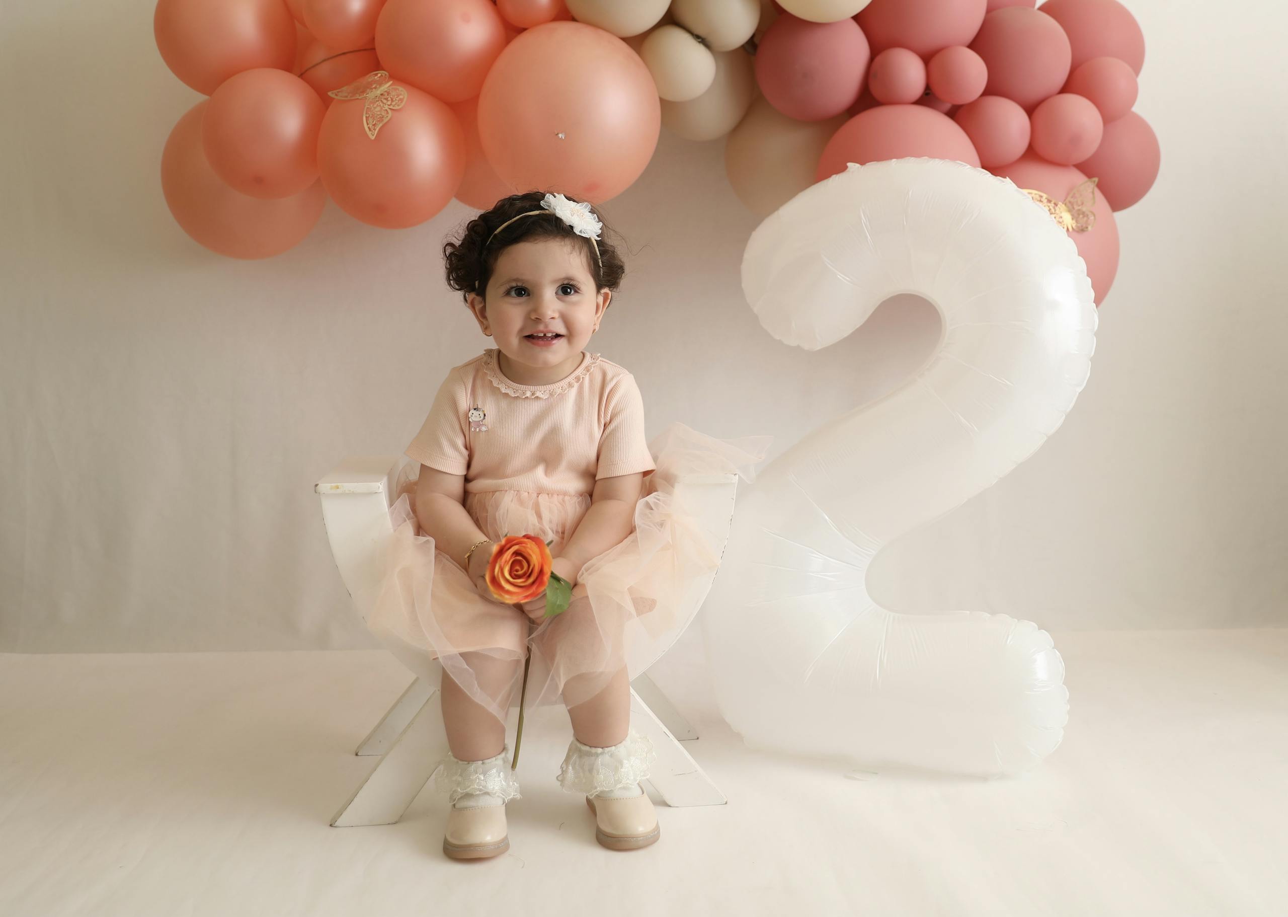 Charming toddler in peach dress with balloons for her second birthday.