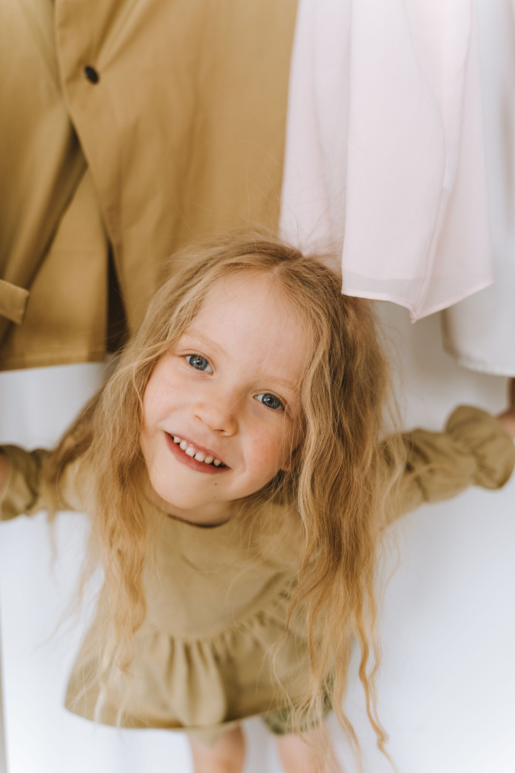 A young girl happily plays and smiles while standing under hanging clothes.